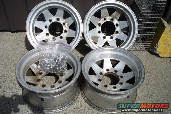 Four aluminum alloy wheels with lug nuts in a plastic bag