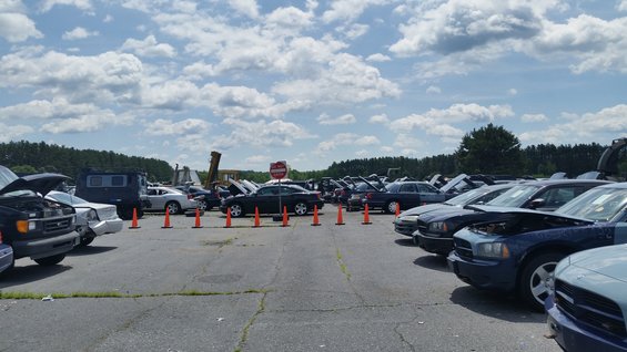 Cars lined up in a lot under a cloudy sky. Some have hoods open