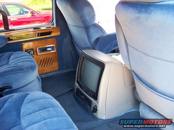 Van interior with blue velour seats, wood trim, and a TV/VCR combo unit