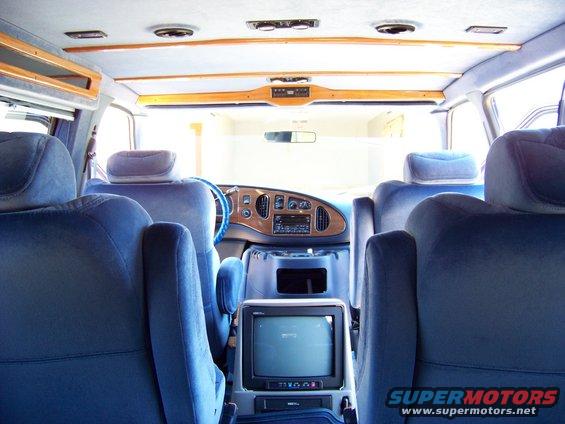 Interior view of a van with blue seats, wood trim dashboard, and a small TV