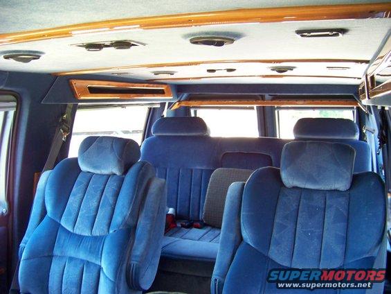 Interior view of a van showing blue velour seats and wood trim on the ceiling