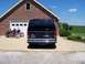 2000 Ford E150 - A dark blue Ford E150 van is parked in front of a garage, with two motorcycles to its left.