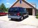 2000 Ford E150 - Rear view of a dark blue Ford E150 van with two-tone blue trim, parked in a driveway next to a red sedan.