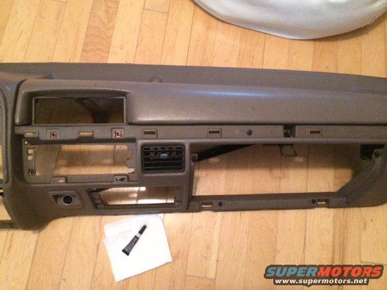 Tan dashboard with air vents and radio/storage slots. Tube of adhesive and cloth on floor