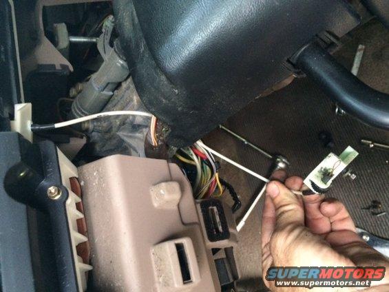 Close-up of car interior wiring harness and fuse box with a hand holding a wire connector