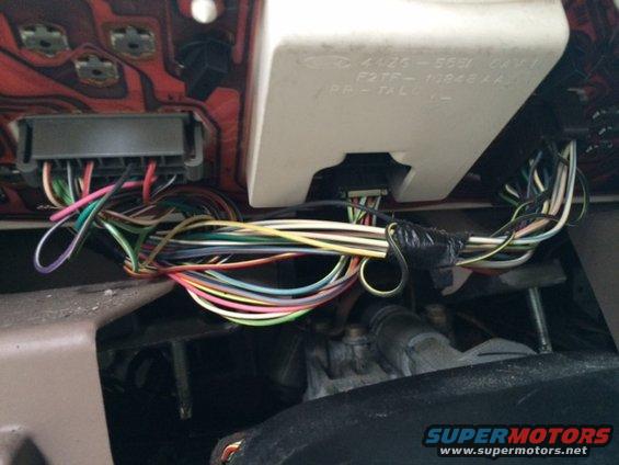 Close-up of a tangled mess of colorful wires connected to a vehicle's dashboard, with some text visible on a white plastic housing