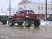 1981 Ford Bronco - A lifted red pickup truck with a roll bar is seen in a muddy, snowy environment, next to another vehicle.