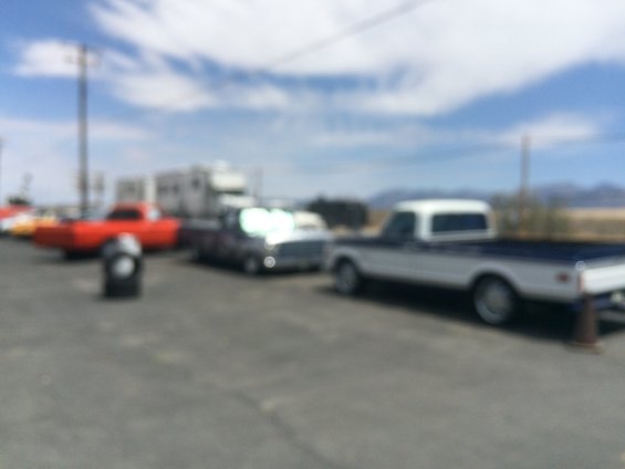 Several vehicles parked outdoors, including a red car, a dark pickup, and a white and blue pickup