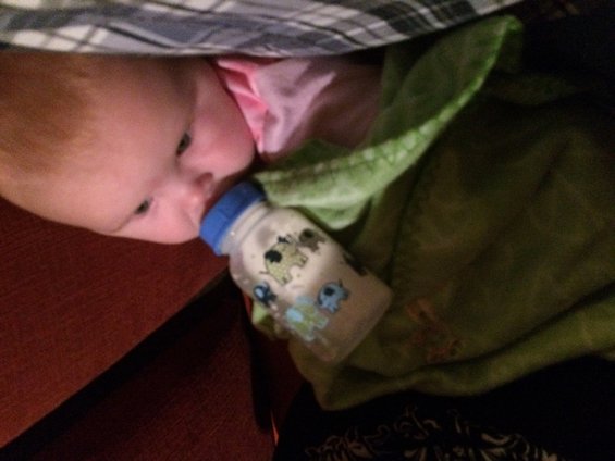 Baby with a bottle, wrapped in a green blanket