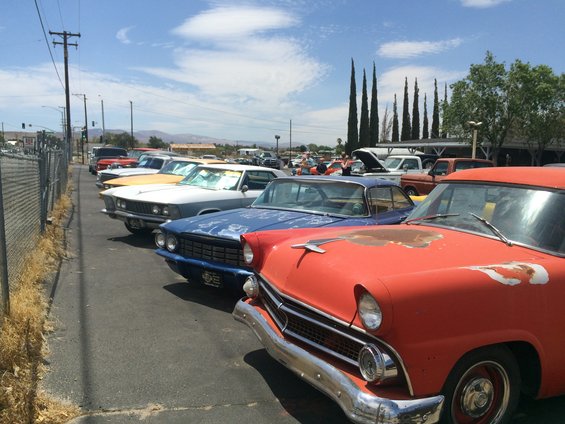Red classic car front end with chrome bumper and grille. Multiple cars parked in lot