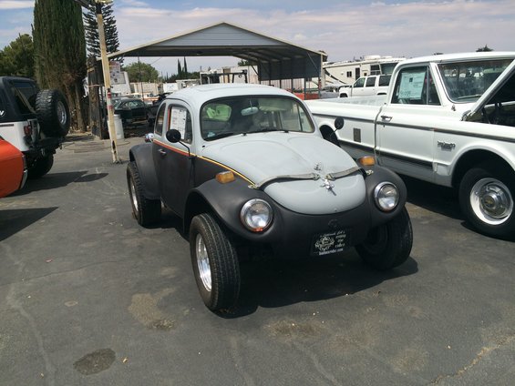 Modified VW Beetle with wide fenders and off-road tires parked next to a white pickup truck