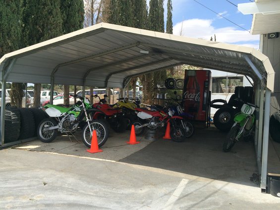Green dirt bike parked under carport next to tires and a Coca-Cola machine