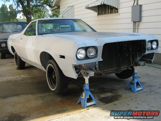 Car on jack stands, front end disassembled. Another vehicle parked behind it