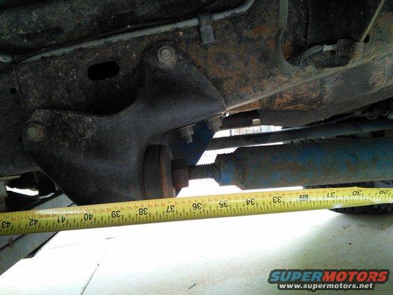 Undercarriage suspension component with a yellow measuring tape showing approximately 33-43 inches