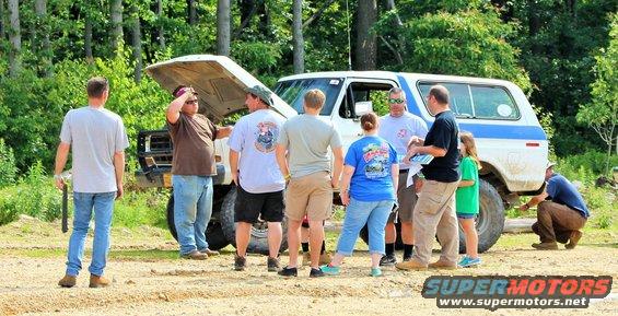 White SUV with hood open, group of people standing around it outdoors