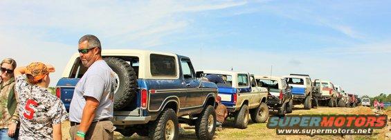 Blue and white 1978 Ford Bronco with spare tire on rear, parked in a line of off-road vehicles