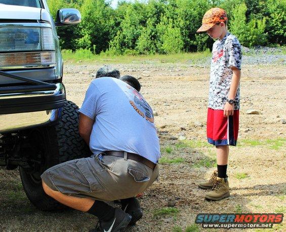 Front view of a dark-colored truck with a man changing the tire
