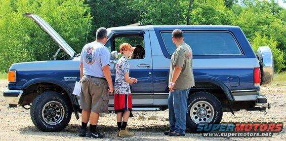 Blue and silver Ford Bronco with hood open, three people standing around it
