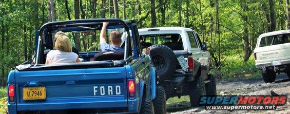 Blue 1979 Ford Bronco rear view with license plate AL7946, driving on a dirt road with two other Broncos