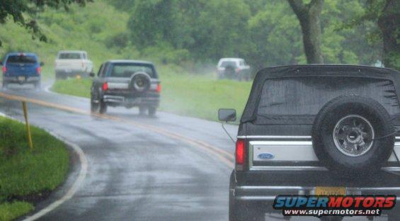 Black Ford Bronco with soft top and spare tire on rear, driving on wet road