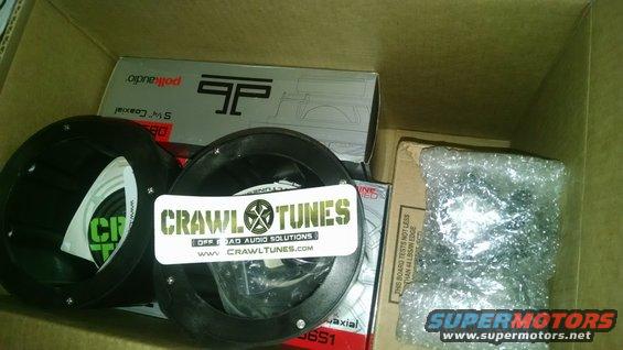 Two black car audio speakers and boxes with 'CrawlTunes' and 'Polk Audio' branding inside a cardboard box
