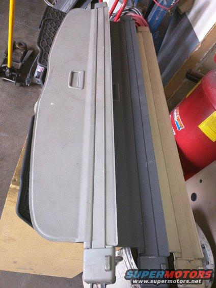 Gray car cargo cover with black trim, lying flat on a wooden surface