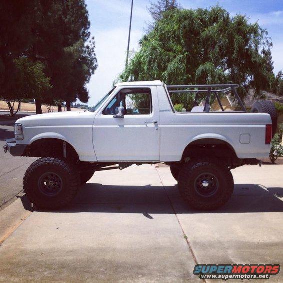 White SUV with lifted suspension and off-road tires parked on a sidewalk
