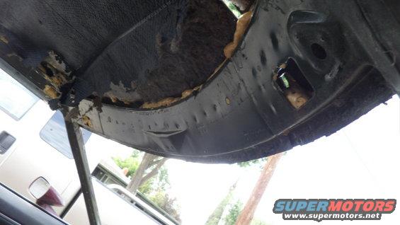 Underside of a car's body panel with insulation exposed and some rust