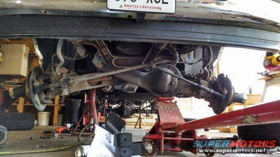 Rear axle assembly of a 1990s SUV on jack stands, showing differential, brake drums, and suspension links