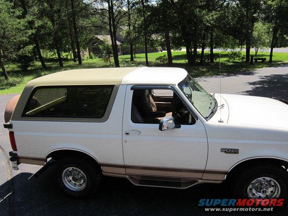 White 1994 Ford Bronco with tan roof and brown trim, seen from the side at a 3/4 front angle