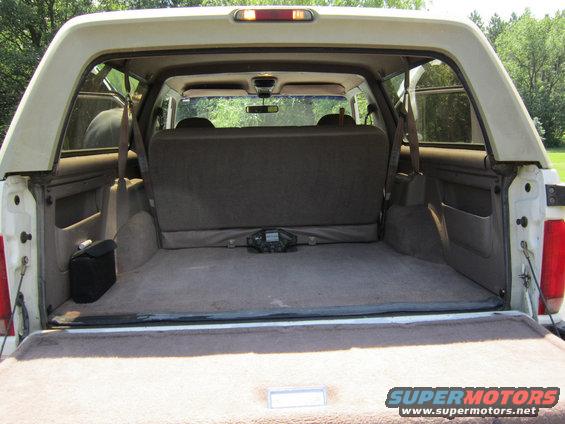 White Ford Bronco interior cargo area, open tailgate, folded rear seat, black bag on left