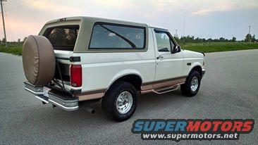 White 1994 Ford Bronco with tan top and spare tire on back, parked on asphalt road