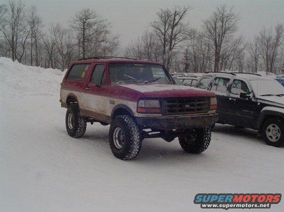 Red and white 1994 Ford Bronco with lifted suspension parked in snow