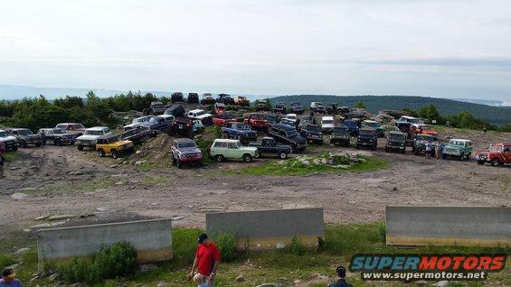 Many off-road vehicles gathered on a rocky hilltop under a cloudy sky