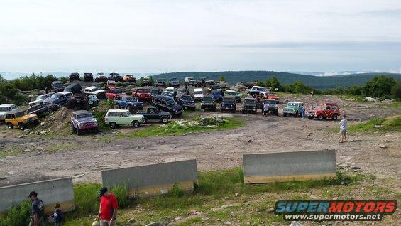 Lots of SUVs and trucks parked on a rocky hill with a view of distant mountains
