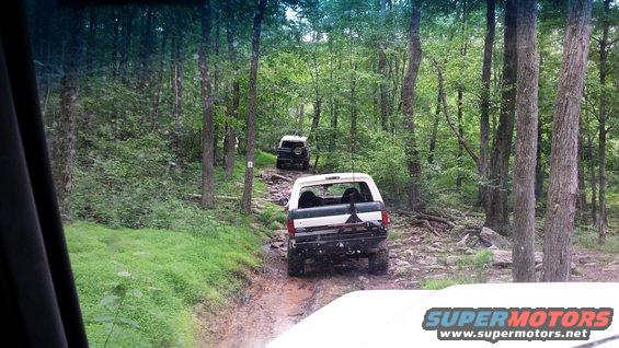 White Ford Bronco driving on a rocky, wooded trail with another Bronco behind it