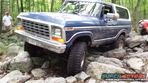 Blue 1978 Ford Bronco navigating a rocky trail with trees in the background