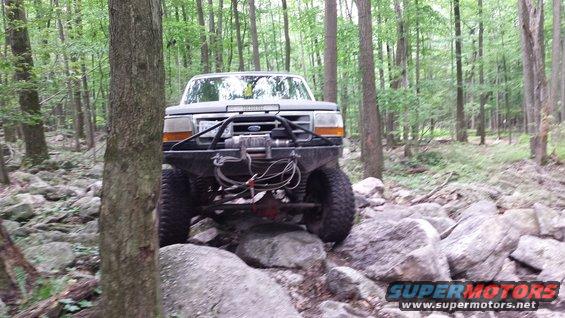 Modified truck with winch and bull bar driving over rocks in a forest