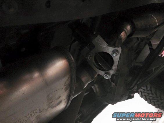 Close-up of a vehicle's exhaust system, showing a flange and part of the muffler. Text on the muffler reads 'MAGNAFLOW'