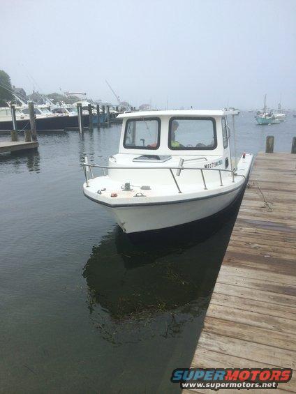 White boat with a cabin, docked at a wooden pier. Registration number M1070WB is visible