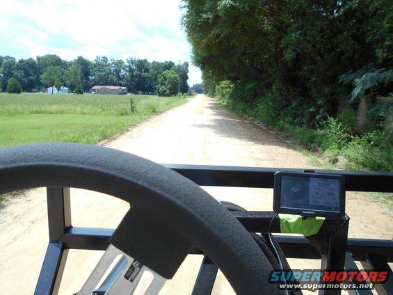 View from a vehicle's interior showing a steering wheel and a Garmin GPS unit mounted on a frame, looking down a dirt road