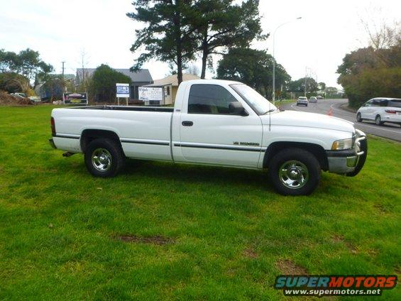 White pickup truck parked on grass, side view. Chrome wheels, bull bar on front