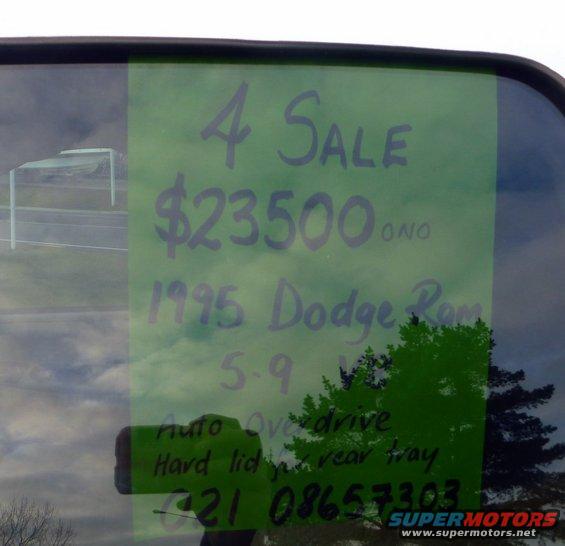 Handwritten 'For Sale' sign on a car window lists a 1995 Dodge Ram for $23,500