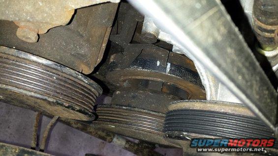 Engine pulleys and belts, some are rusty. A white mark is visible on one pulley