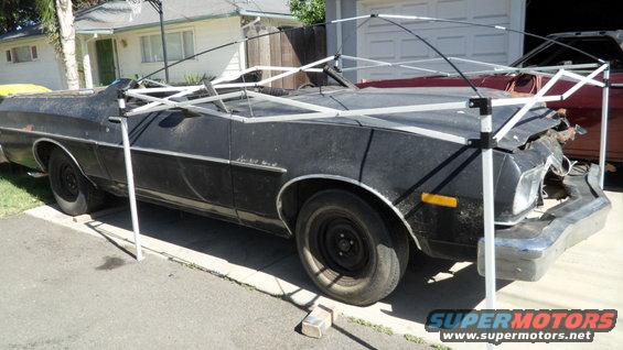 Black 1972 Ford Ranchero with front-end damage, covered by a canopy