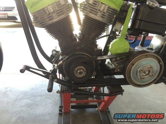 Motorcycle engine with green tape on cylinders, on a red lift. Belt drive visible