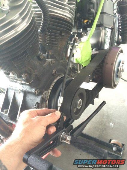 Close-up of a motorcycle's V-twin engine and belt drive system with a hand adjusting a cable