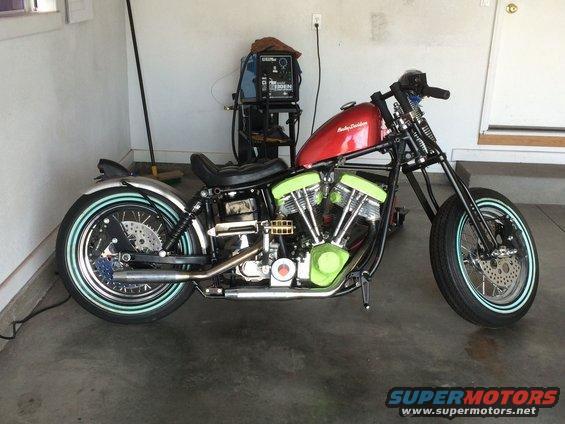 Red Harley-Davidson motorcycle with green engine covers and whitewall tires, parked indoors