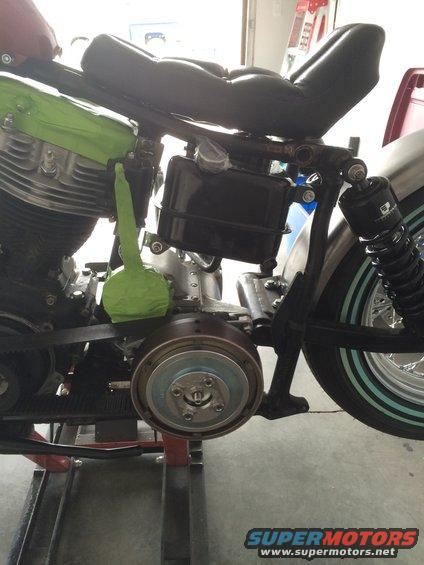 Close-up of a motorcycle engine, frame, seat, and rear wheel assembly. Green tape covers part of the engine