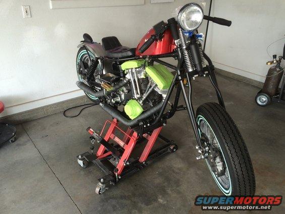 Motorcycle on a red lift with green padding on the engine. Red gas tank, black seat, and black exhaust pipes